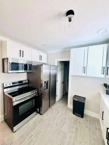 Kitchen featuring appliances with stainless steel finishes, white cabinets, wood tiled floors, crown molding, and light stone counters