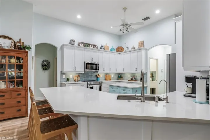 Kitchen featuring a peninsula, white cabinetry, arched walkways, light stone counters, and stainless steel appliances