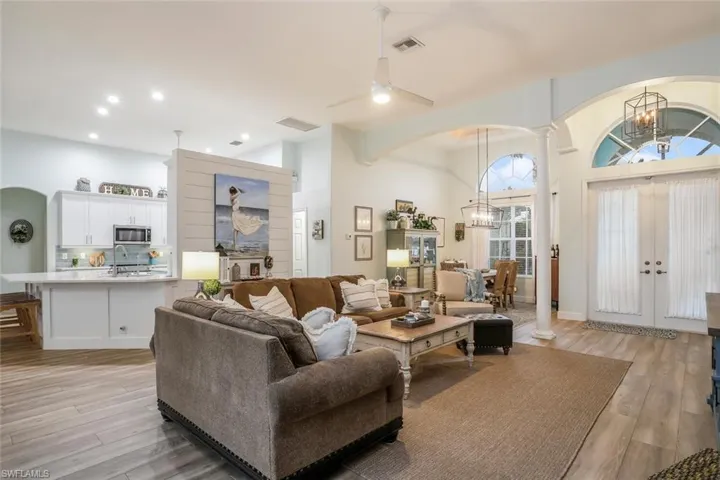 Living/Family room with arched walkways, light wood-style floors, ornate columns, a chandelier, and a high ceiling