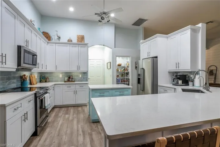White kitchen with stainless steel appliances, a peninsula, decorative backsplash, a kitchen breakfast bar.