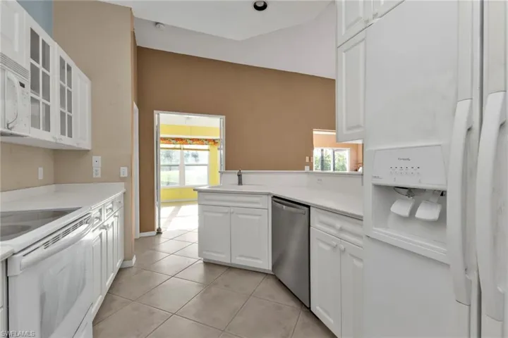 Kitchen featuring white appliances, white cabinetry, light tile patterned floors, and kitchen peninsula