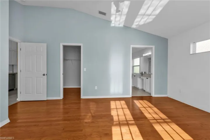 Unfurnished bedroom with connected bathroom, a walk in closet, multiple windows, and light wood-type flooring