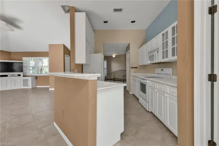 Kitchen featuring a kitchen breakfast bar, white cabinetry, light tile patterned flooring, and white appliances