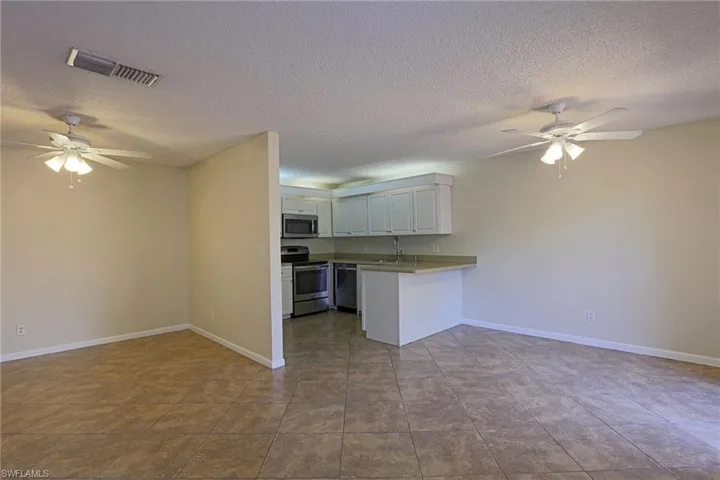 Kitchen with ceiling fan, open floor plan, stainless steel appliances, white cabinetry, and a textured ceiling