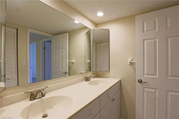 Bathroom with a closet, a textured ceiling, double vanity, and recessed lighting
