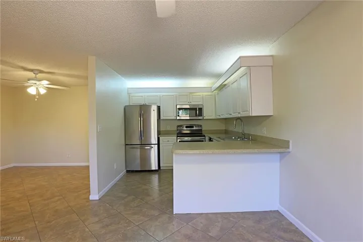 Kitchen with ceiling fan, stainless steel appliances, a peninsula, a textured ceiling, and white cabinetry