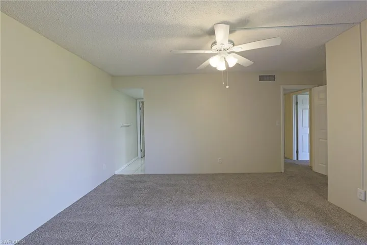 Empty room featuring light carpet, a ceiling fan, and a textured ceiling