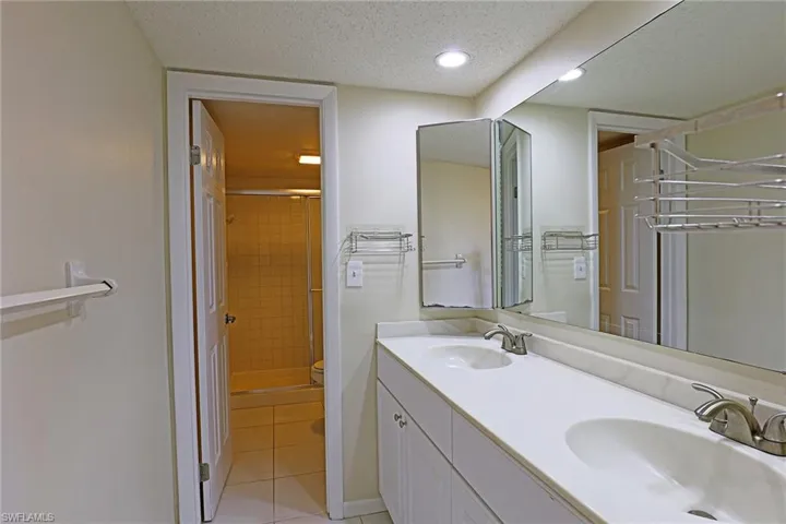 Bathroom with a textured ceiling, double vanity, a shower stall, light tile patterned floors, and recessed lighting