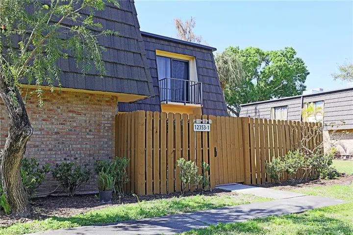View of side of property with brick siding, a balcony, a gate, and mansard roof