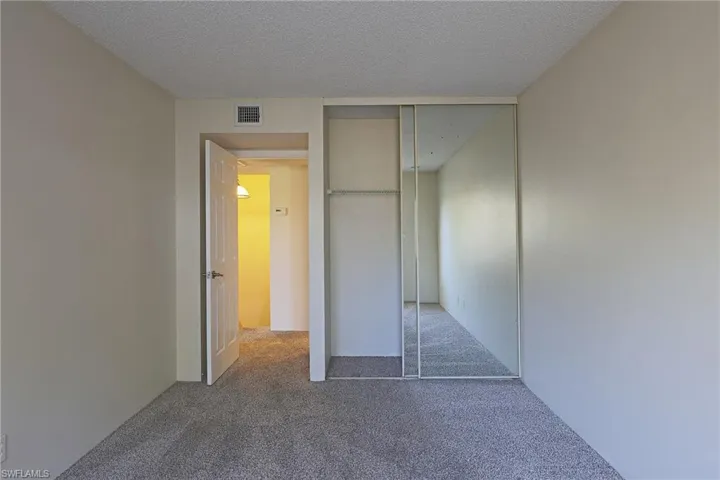 Unfurnished bedroom with a textured ceiling, dark carpet, and a closet