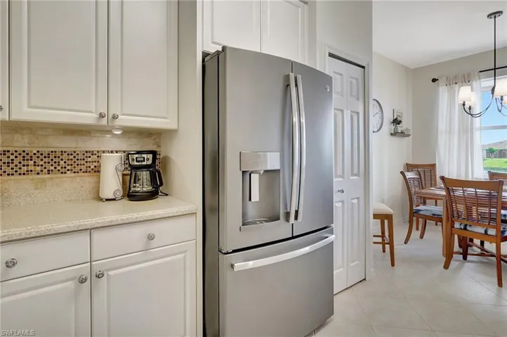 Kitchen featuring tasteful backsplash, decorative light fixtures, stainless steel fridge, and white cabinets