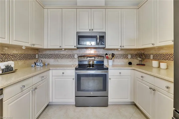 Kitchen with stainless steel appliances, white cabinetry, light tile patterned floors, and decorative backsplash