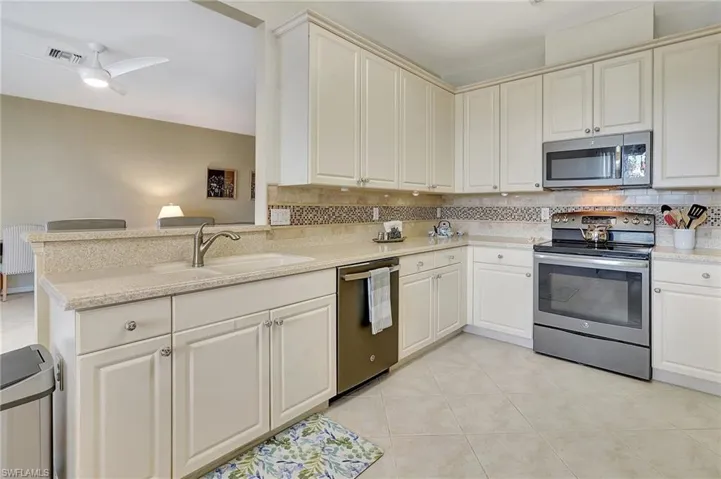 Kitchen featuring sink, light tile patterned floors, backsplash, stainless steel appliances, and kitchen peninsula