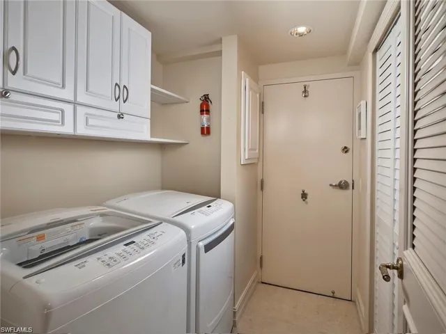 Laundry room with light tile patterned flooring, washer and clothes dryer, and cabinets
