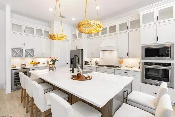 Kitchen featuring appliances with stainless steel finishes, a kitchen breakfast bar, light stone counters, recessed lighting, and wine cooler