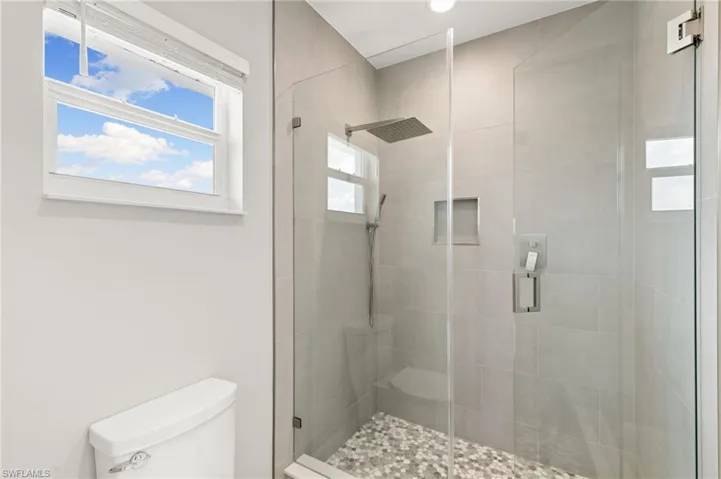 A walk in shower with full-height tiling, beveled glass, and dual shower heads.