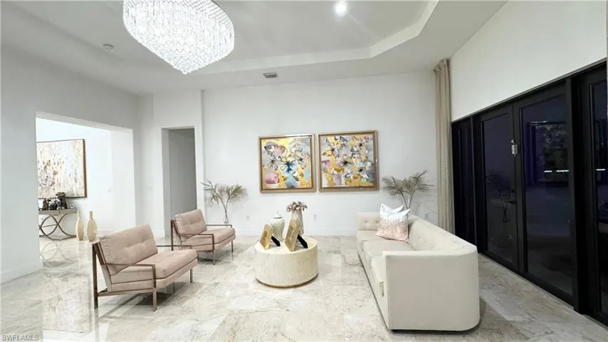 Living area featuring a tray ceiling, a chandelier, and marble tiled floors