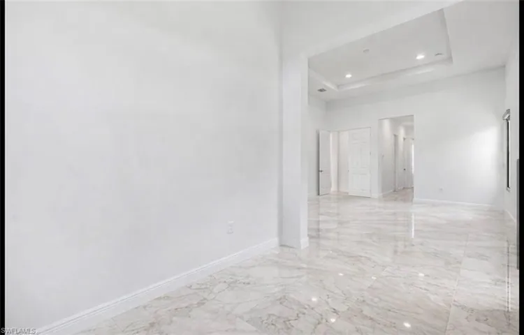 Empty room featuring a tray ceiling, light marble finish flooring, recessed lighting, and a towering ceiling