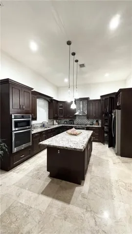 Kitchen featuring dark brown cabinets, a center island, decorative light fixtures, light stone countertops, and stainless steel appliances