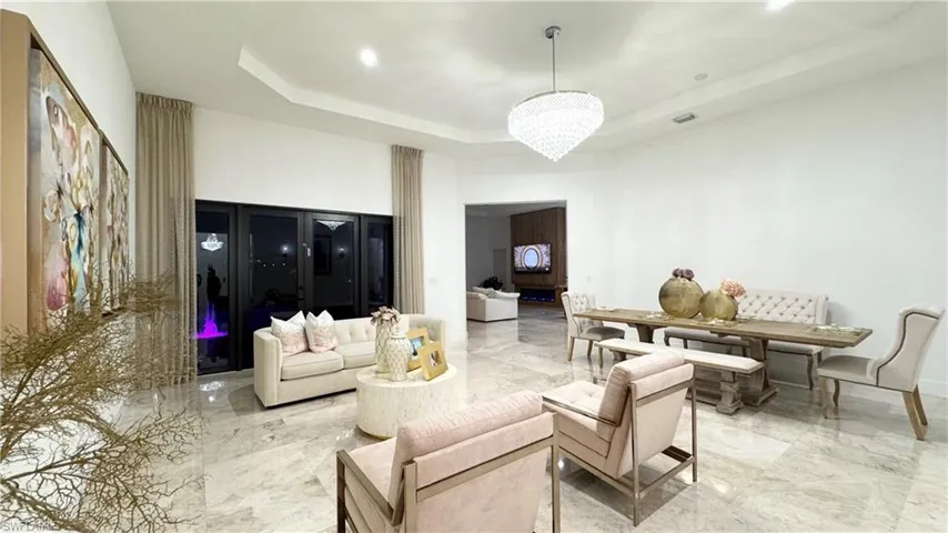 Living area with a tray ceiling, light marble finish flooring, a chandelier, and recessed lighting
