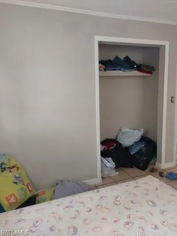 Tiled bedroom with a closet, crown molding, and baseboards