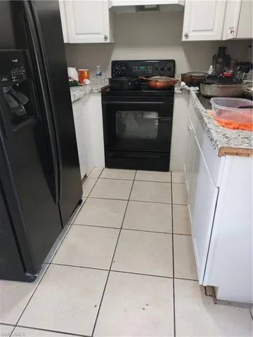 Kitchen with fridge, range, white cabinetry, and light countertops