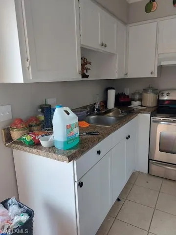 Kitchen with electric stove, a sink, under cabinet range hood, white cabinets, and light tile patterned floors
