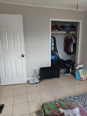Unfurnished bedroom featuring crown molding, tile patterned floors, a closet, and baseboards