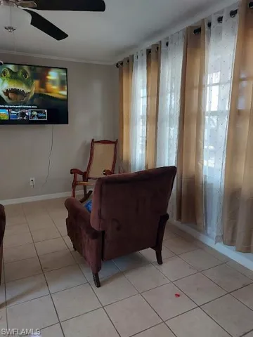 Living area featuring light tile patterned floors, ceiling fan, and crown molding