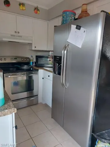 Kitchen with appliances with stainless steel finishes, under cabinet range hood, crown molding, white cabinetry, and light tile patterned floors