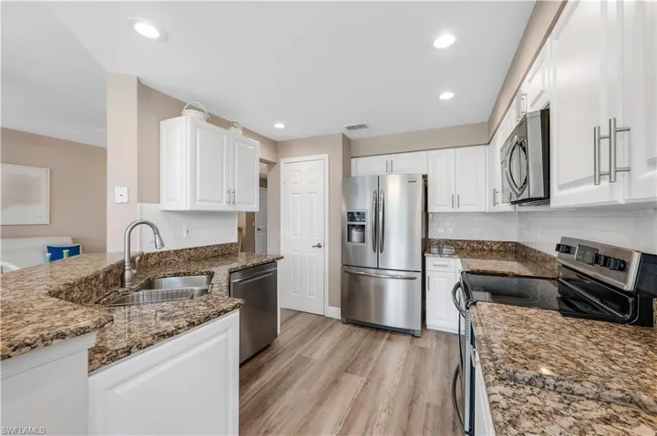 Kitchen featuring appliances with stainless steel finishes, white cabinets, granite counters, light wood-look LVP floors, and recessed lighting