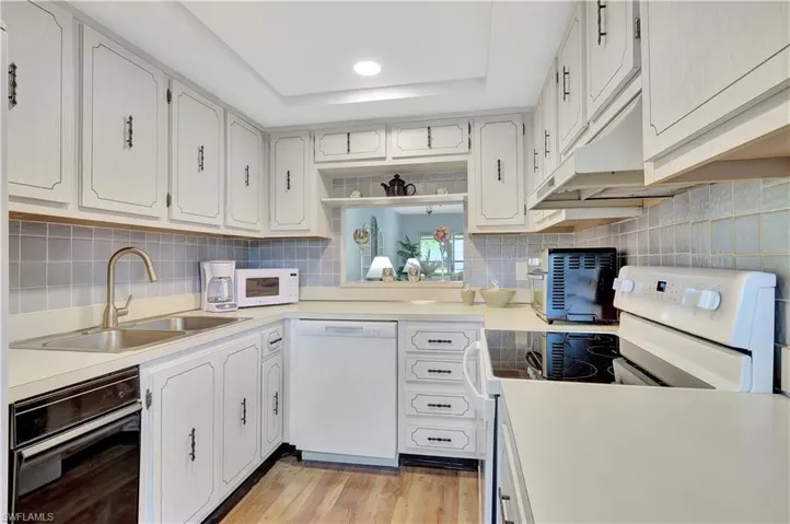 Kitchen featuring tasteful backsplash, a tray ceiling, white appliances, a sink, and light wood look vinyl floors