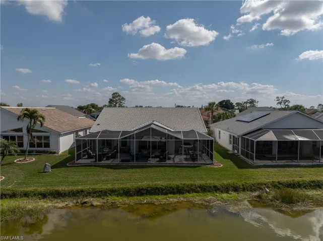 Rear view of house with a water view, glass enclosure, and a lawn