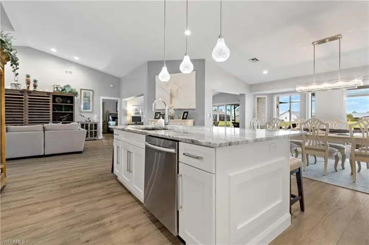 Kitchen with sink, light stone counters, decorative light fixtures, dishwasher, and white cabinets