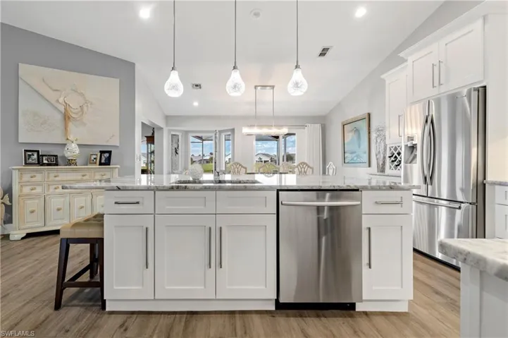 Kitchen with stainless steel appliances, white cabinetry, and hanging light fixtures