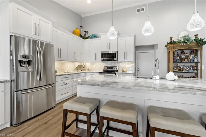 Kitchen with a breakfast bar area, appliances with stainless steel finishes, white cabinetry, light stone counters, and decorative light fixtures