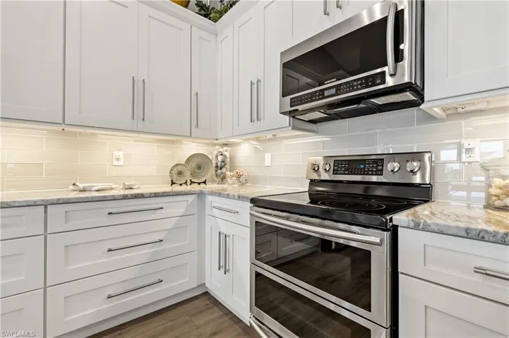 Kitchen with backsplash, appliances with stainless steel finishes, light stone counters, and white cabinets
