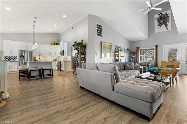 Living room with high vaulted ceiling, sink, light hardwood / wood-style flooring, ceiling fan, and french doors
