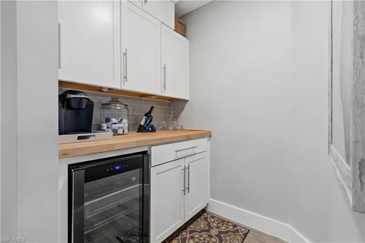Bar featuring hardwood / wood-style flooring, wooden counters, tasteful backsplash, white cabinets, and beverage cooler
