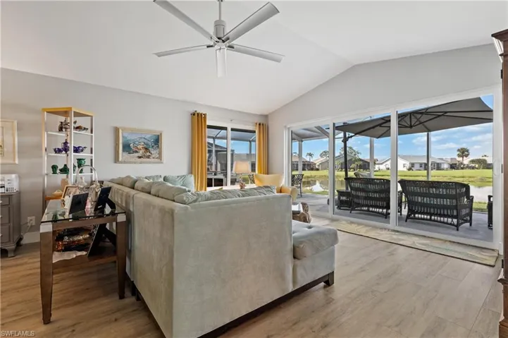 Living room with lofted ceiling, a water view, ceiling fan, and light wood-type flooring