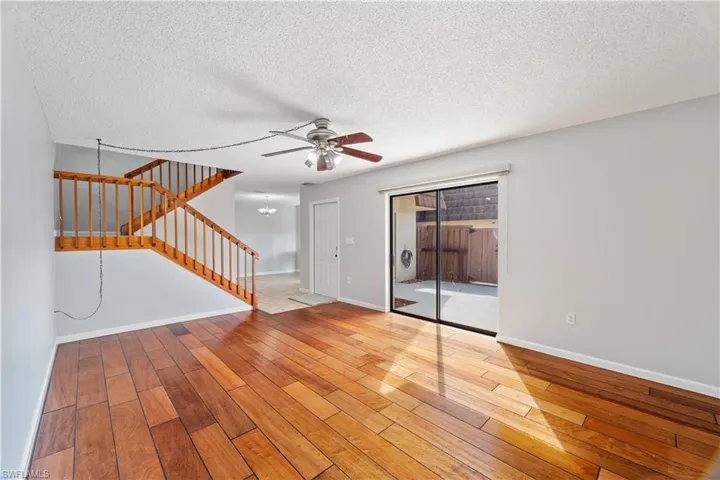 Unfurnished living room featuring a textured ceiling, a ceiling fan, hardwood / wood-style floors, and stairs