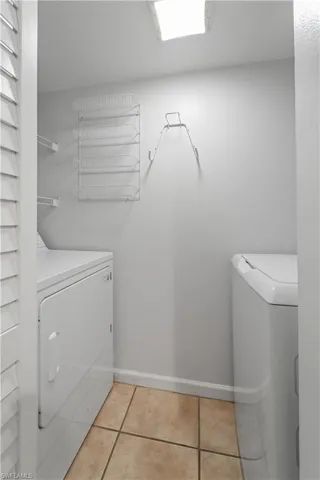 Clothes washing area with laundry area, separate washer and dryer, light tile patterned floors, and baseboards