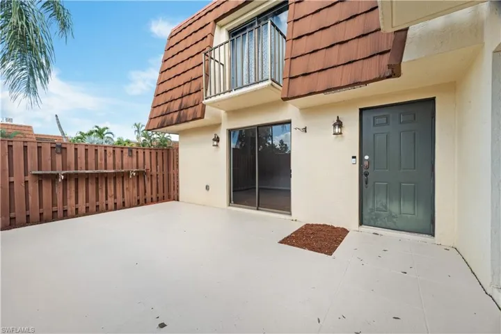 Doorway to property featuring mansard roof, fence, a patio, a balcony, and stucco siding