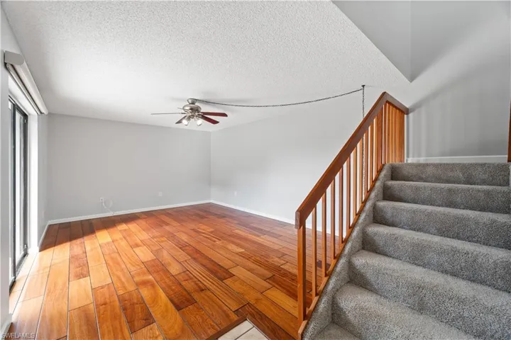 Stairs featuring a textured ceiling, baseboards, a ceiling fan, and wood finished floors