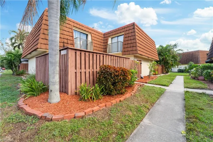 View of side of home featuring a yard, mansard roof, and stucco siding