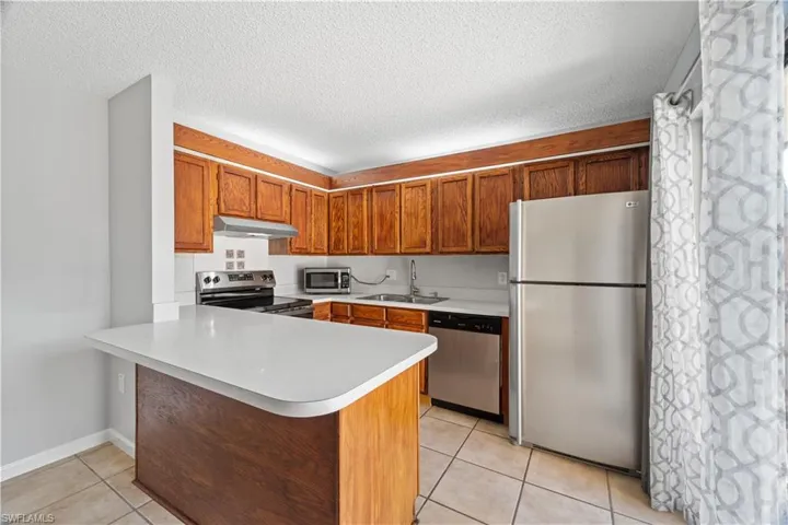 Kitchen featuring a sink, a peninsula, under cabinet range hood, stainless steel appliances, and light tile patterned flooring