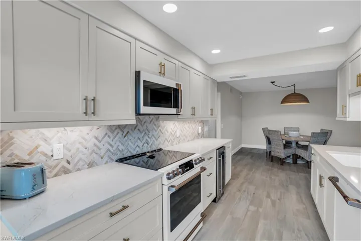 Kitchen with backsplash, white cabinets, white appliances, and light hardwood / wood-style flooring