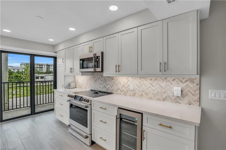 Kitchen with wine cooler, tilelight hardwood / wood-style flooring, electric range, backsplash, and white cabinetry