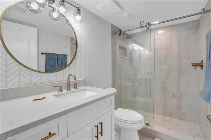 Bathroom featuring a shower with shower door, toilet, and large vanity