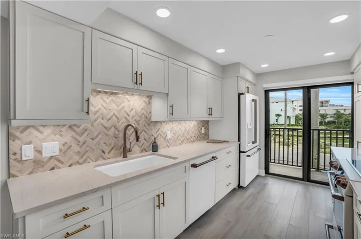Kitchen featuring white cabinets, light hardwood tile/ wood-style floors, backsplash, high end white refrigerator, and sink